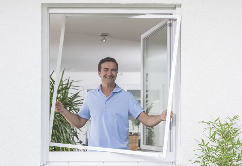 Person montiert Insektenschutzspannrahmen an einem Fenster